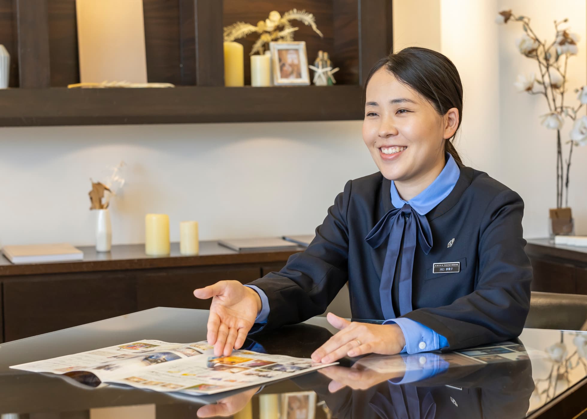 紺色と水色の制服姿でカタログを開いて接客中の小金丸さん