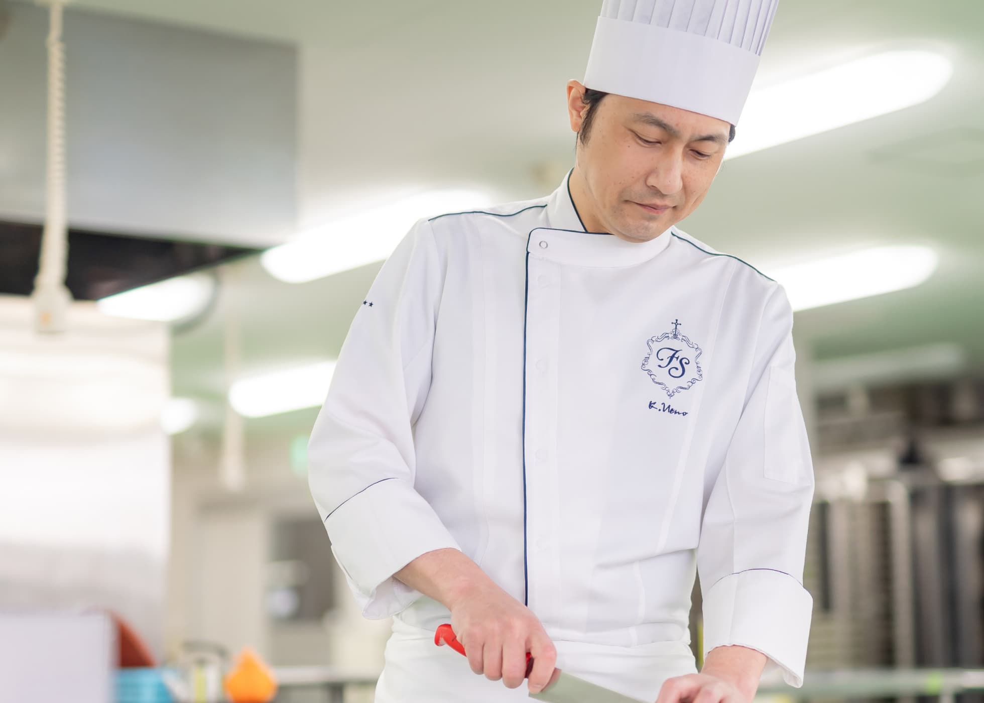 白いコックコートとコック帽姿で包丁をもち調理中の上野さん