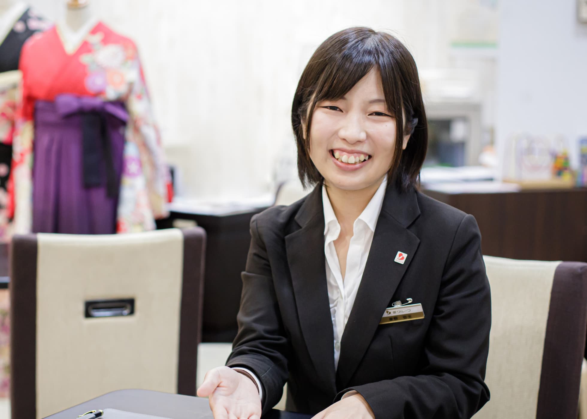 スーツ姿で正面に笑顔を向けて接客中の東野さん